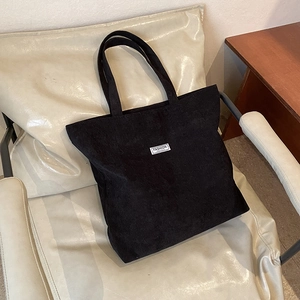 Detail of black corduroy tote bag with fashion label on a light neutral chair