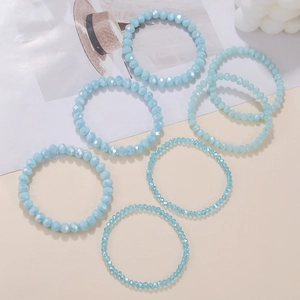 Makro-Detail eines 7-teiligen hellblauen Kristallperlen-Armbandsets vor sommerlichem Hintergrund