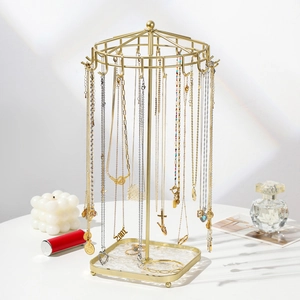 Rotating gold metal jewelry organizer stand for necklaces and bracelets on white surface