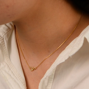 Close-up of heart and infinity pendant necklace with white diamonds on female neck