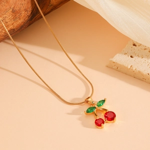 Detail view of a gold cherry pendant necklace with red and green crystals on stone decor