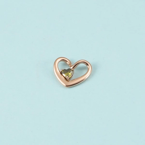 Pendentif cœur en or rose avec cristal vert olive sur fond bleu clair en gros plan