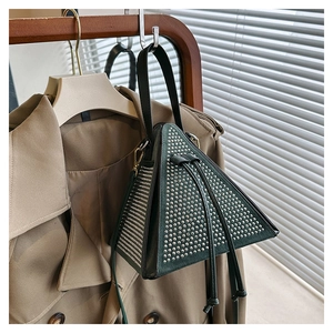 Detailed close-up of dark green triangular bucket bag with rivets on trench coat