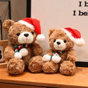 Christmas teddy bear plush toy with festive red scarf and hat on wooden surface