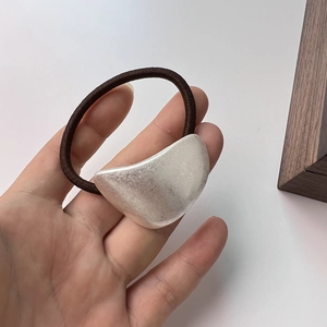 Macro shot of minimalist matte silver crescent moon hair tie with brown elastic rope