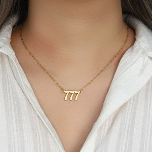 Golden stainless steel number 777 pendant necklace worn on a model in a white shirt