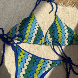 Détail d'un bikini crocheté avec motifs à vagues bleues et liens tressés sur tapis