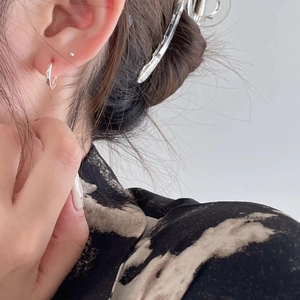 Close-up of twisted 925 silver hoop earrings and studs worn on a model's ear
