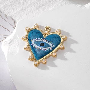 Detail of heart evil eye charm with blue enamel, pearls and gold trim on textured background