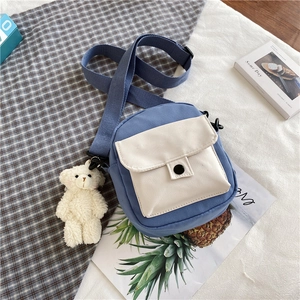 Détail d'un sac bandoulière en toile bleu et beige avec un pendentif ours en peluche
