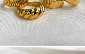 Close-up of gold stainless steel rings with spiral and ribbed textures on white fabric
