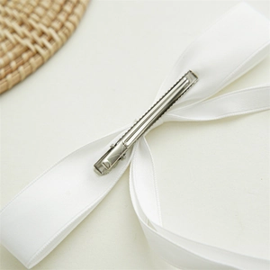 Close-up of the silver metal alligator clip on the back of a white satin bow hair ribbon