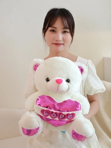 Detailed close-up of white plush teddy bear with a pink metallic heart and LOVE embroidery