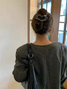 Dettaglio di un fermaglio per capelli a cuore nero glitterato con perla su capelli castani