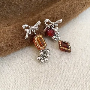 Asymmetric bow drop earrings with amber and red beads on warm textured fabric