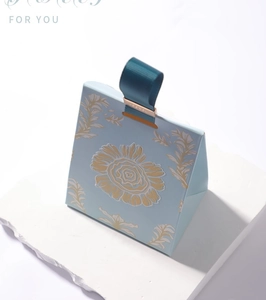Detail view of light blue trapezoid gift box with gold floral embossing and blue handle