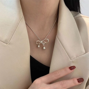 Elegant silver bow pendant necklace with snake chain worn on a chic cream blazer
