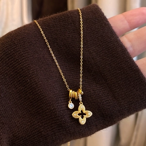 Détail du pendentif trèfle doré et cristal sur un pull en maille marron chaud