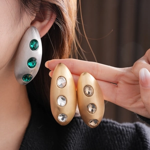 Detailed view of silver and gold brushed oval earrings with green and white gemstones