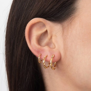 Three sizes of gold twisted rope hoop earrings worn by a model in a minimal studio setting