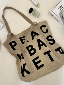 Minimalist khaki canvas tote bag with black Peace Basket lettering on a white desk