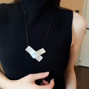 Detail of white geometric crisscross pendant on a black cord worn over a sweater