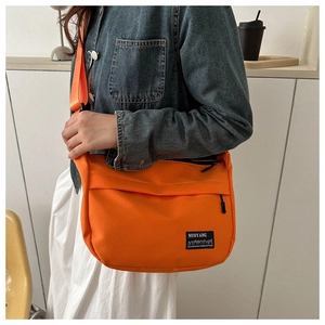 Detail of orange nylon shoulder bag with woven label on blue denim jacket background