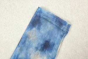 Macro detail of blue tie-dye mesh fabric showing neat double-stitch hem and texture