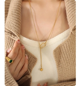 Detail of 18k gold plated ball tassel necklace and green gemstone ring on knitwear