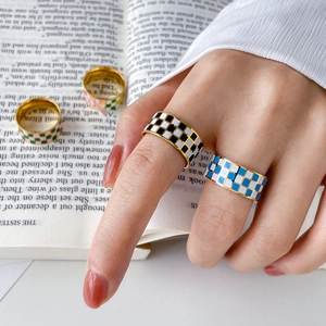 Detail of colorful checkerboard enamel rings on gold bands worn on hand over a book