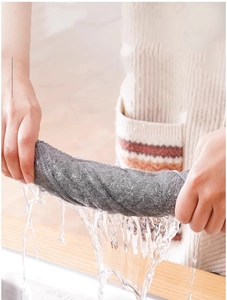 Close-up of hands wringing out gray bamboo fiber dishcloth with water dripping into a sink