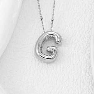 Macro detail of silver G balloon pendant with polished metallic luster on white texture