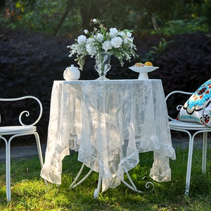 Elegante tovaglia in pizzo bianco con motivi floreali e bordi a balze su tavolo tondo