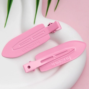 Close-up of pink seamless metal hair clips on a ceramic tray with green leaves