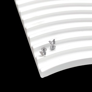Macro shot of silver butterfly stud earrings on a geometric display stand with black background