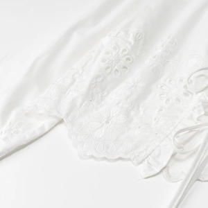 Detailed close-up of intricate floral embroidery and hollow-out design on white cotton blouse