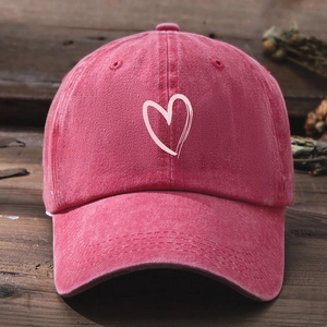 Close-up of vintage washed red baseball cap with white heart embroidery on wood background