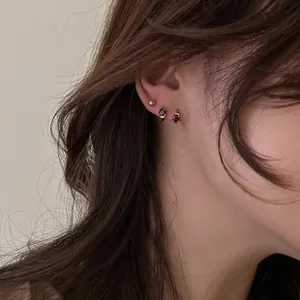 Close-up of gold ear set featuring black gemstone hoops and minimalist metal studs