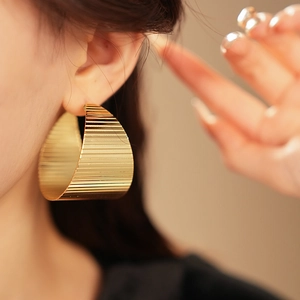 Detailed view of large gold hoop earrings with vertical grooved metal texture and shine