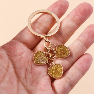 Close-up of golden keychain with three heart pendants filled with sparkling gold glitter