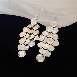 Close-up of tiered silver metal discs on dangling hook earrings with a polished finish