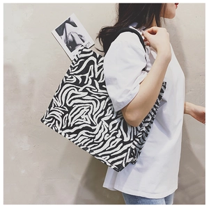 Detail of a zebra print canvas tote bag with black strap worn by a model