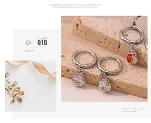 Detail shot of silver zircon earrings with orange gemstones on a textured stone surface