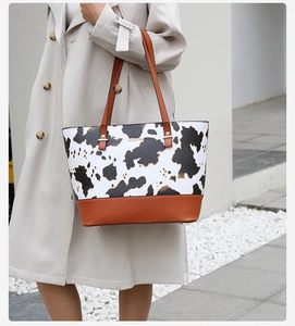 Detail of a large cow print tote bag with brown leather handles worn by a model