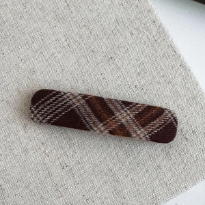 Detail of a brown plaid tweed rectangular hair clip on a natural linen background