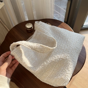 Détail de la texture d'un cabas en tweed crème sur table en bois sous le soleil
