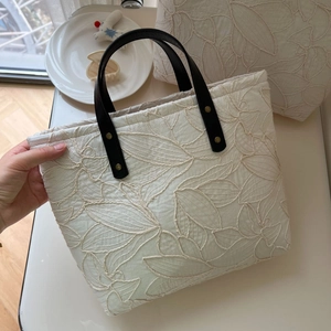 Detail of cream canvas tote bag with leaf embroidery, black leather handle and gold rivets