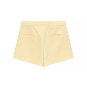 Flat lay of pale yellow high-waisted shorts with decorative back welt pockets