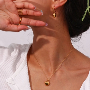 Close-up of golden heart pendant necklace, earrings, and minimalist rings on model