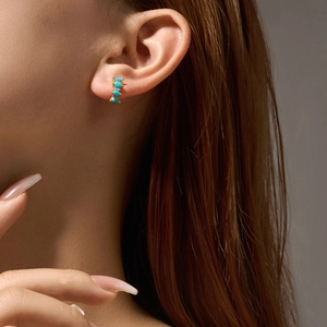 Eleganti orecchini d'oro con pietre turchesi indossati da una modella di profilo